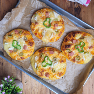 a photograph of 4 mini pizzas on parchment paper on a baking tray sitting on top a kitchen worktop