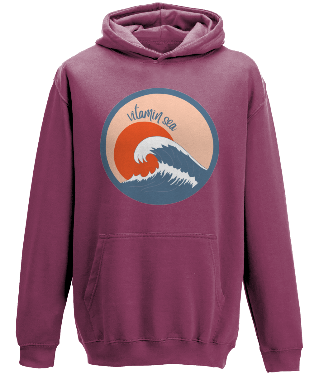 A photo of a plum kids hoodie with a round Vitamin Sea design featuring a large wave in front of a low orange sun