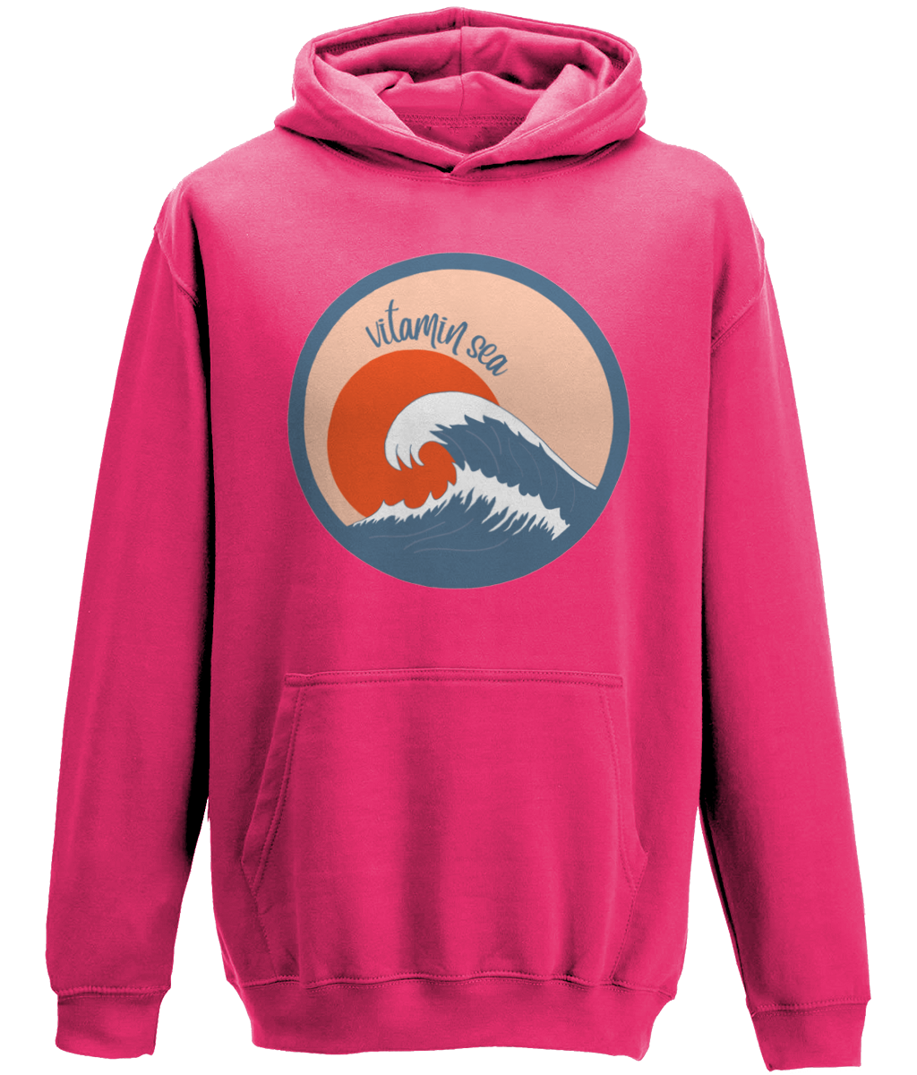 A photo of a hot pink kids hoodie with a round Vitamin Sea design featuring a large wave in front of a low orange sun